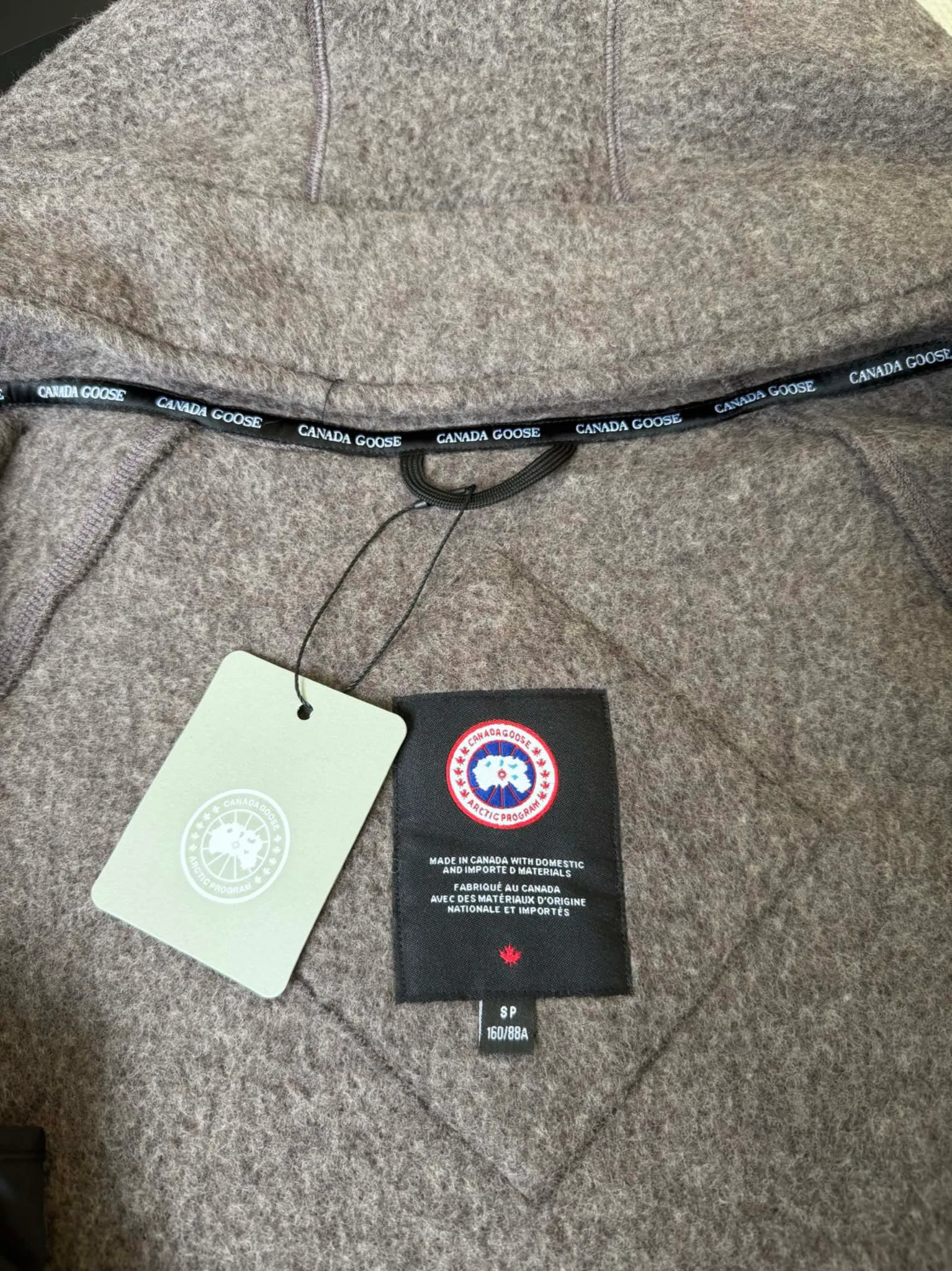 P660 Canada Goose Fleece Wool Hooded Jacket Fabric selection: Wool fleece fabric blended with wool as the main body and a very small amount of spandex and polyester fiber. Wool is a core natural ingredient that provides unparalleled temperature regulation, antibacterial and anti-odor properties and a skin-friendly feel. The feeding of a small amount of spandex gives the fabric a certain degree of four-way elasticity, making it non-restrictive during daily activities. As the basis of fleece's structure, polyester fiber enhances the fabric's durability, wrinkle resistance and quick-drying properties. It contributes to the loft of the fleece and provides functions such as trapping air.  Detail 1: The sleeves and hem are closed with 2×2 ribbing. Its strong elasticity can closely fit wrists and waists of different thicknesses, forming an effective 'seal' to prevent cold wind from blowing back. It can still maintain its original shape after repeated stretching and use, and is not easy to loose and deform. And the ribbed cuffs can convey a sense of design and enhance the visual beauty.  Detail 2: The combination of hood design and elastic buckle improves warmth and windproof performance when wearing. Accessories: Customized elastic drawstring, elastic buckle, custom zipper pendant, custom armband Size: S M L Color: black gray coffee rice pink